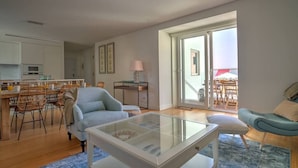A modern living room with a glass coffee table, a dining area with wicker chairs, and a view through large sliding glass doors.