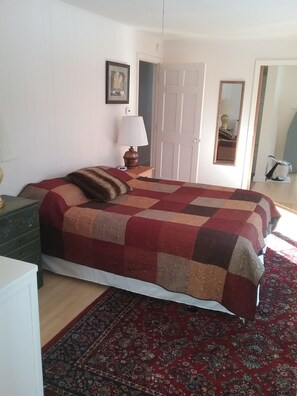 A bedroom with a bed, a nightstand, a lamp, a dresser, a door, and a mirror. - Oceanfront home on the Schoodic Peninsula (Gouldsboro)