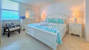 Un dormitorio con una cama, dos mesitas de noche, una silla, un aparador, un espejo y una ventana con persianas.