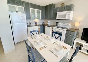 A compact kitchen with a refrigerator, microwave, stove, and dishwasher. There is a dining table set with plates, glasses, and cutlery.