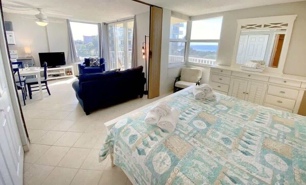 A hotel room with a bed, a desk with a TV, a balcony with a view, and a bathroom with a mirror and cabinets.