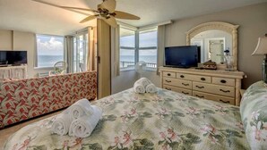 A hotel room with a bed, a television, a dresser, a mirror, and a balcony with a view of the sea.