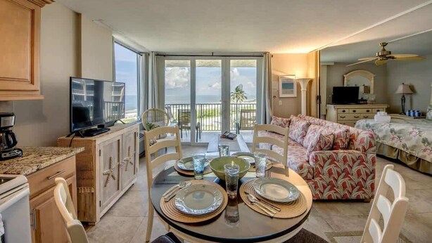 A dining area with a table set for four, a kitchen with a TV, and a balcony with a view.