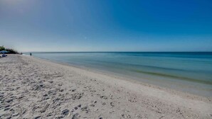 A beach with clear water, a sandy shore, and a few umbrellas.