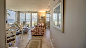 A room with a balcony, a sofa, a dining table with chairs, and a framed picture on the wall.
