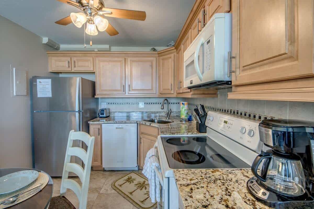 A kitchen with wooden cabinets, a stainless steel refrigerator, a microwave, a stove, and a coffee maker.