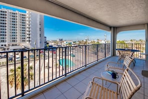Un balcón con vistas a una piscina y edificios, amueblado con sillas y una mesa.