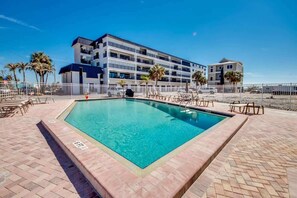 Ein rechteckiger Pool mit einer Fliesenbordüre, umgeben von Liegestühlen und einem weißen Zaun.