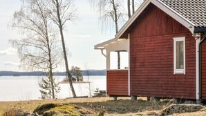 Una pequeña cabaña roja junto a un lago, con una vista despejada del agua y los árboles.