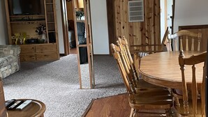 Un comedor con una mesa y sillas de madera, un televisor sobre un mueble de madera y un cartel con la palabra 'Welcome' en la pared.