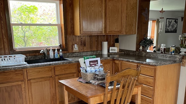 Una cocina con armarios de madera, encimera de granito, una mesa de comedor con una silla y una ventana que da a árboles.