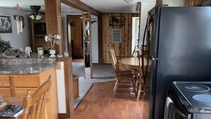 Una cocina con armarios de madera, un refrigerador negro y un comedor con sillas y una mesa de madera.