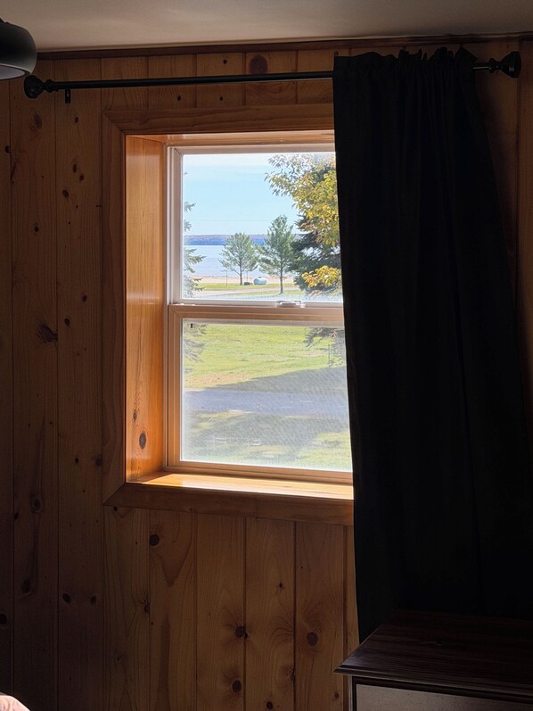 Una habitación con paneles de madera, una ventana que da a una zona verde con árboles y una cortina oscura parcialmente abierta.