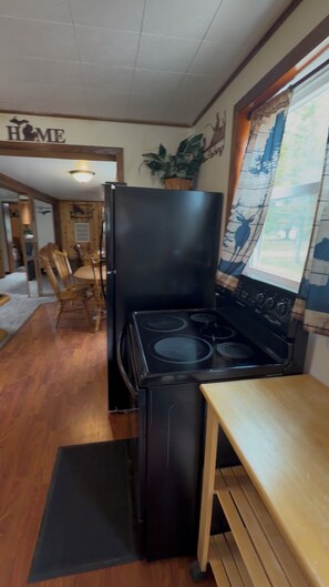 Une cuisine compacte avec un poêle noir, une table à manger en bois et une fenêtre donnant sur une forêt.
