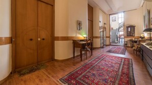 Un pasillo con una puerta de madera, un escritorio con una silla, una alfombra estampada y una escalera que lleva a otra habitación.