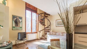 Una sala de estar con una escalera de caracol, televisor, sofá y un ventanal grande.