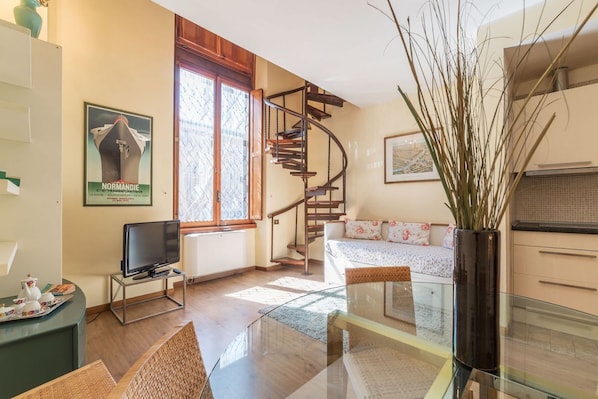 A living room with a spiral staircase, a television, a sofa, and a large window.