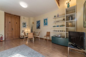 A living room with a dining table, chairs, a TV, shelves with decorative items, and a fire extinguisher.