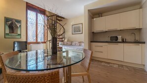 Un comedor con mesa de vidrio y sillas de mimbre, una cocina con muebles blancos y una escalera con vistas.