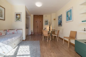 A room with a sofa, a dining table with chairs, a green cabinet, and artwork on the walls.