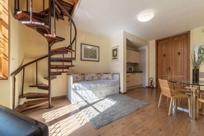 A spiral staircase, a sofa with floral cushions, a dining table with chairs, and a kitchen area.