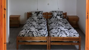 Una habitación con dos camas de madera y ropa de cama con estampado floral blanco y negro, mesitas de noche de madera y un marco de puerta de madera.