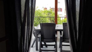 Un espacio de comedor al aire libre con una mesa y sillas, vista a edificios y follaje en el fondo, y una estructura de pérgola de madera.