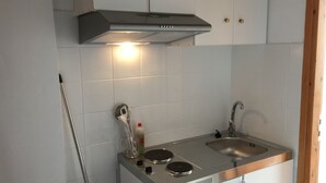 Cocina compacta con dos fregaderos de acero inoxidable, estufa integrada y extractor sobre la hornilla.