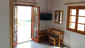 Una habitación con techo de madera, un televisor montado en la pared, un escritorio de madera con cojín y una ventana con marco de madera.