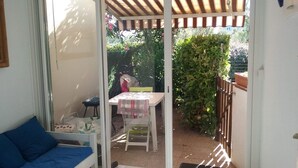 Et værelse med en seng, et lille bord dækket med et stofserviet og en stol. Der er et vindue med udsigt til en have.