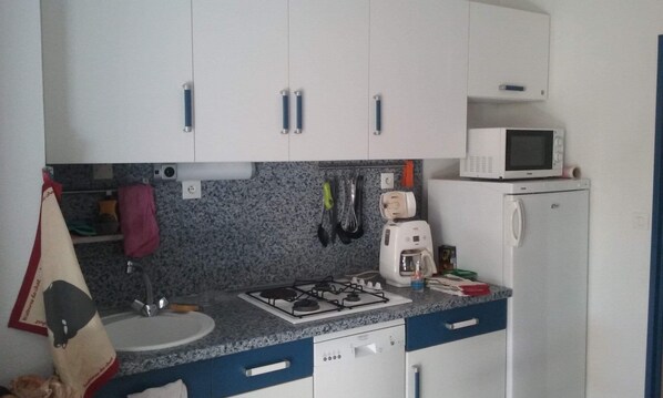 A compact kitchen with white cabinets, a microwave, a gas stove, and a refrigerator.