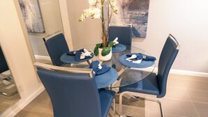 A modern dining area with a glass table surrounded by blue chairs, a vase with white orchids, and a contemporary abstract painting on the wall. - Palm Springs Oasis Getaway with Mtn Views - Near Tram & Uptown. (Palm Springs)
