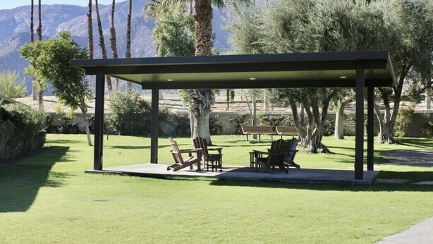 A covered outdoor seating area with chairs and tables, surrounded by greenery and palm trees, with mountains in the background. - Palm Springs Oasis Getaway with Mtn Views - Near Tram & Uptown. (Palm Springs)