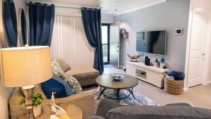 A modern living room with a sofa, a coffee table, and a TV. There is a lamp, a plant, and a basket on the side table. - Palm Springs Oasis Getaway with Mtn Views - Near Tram & Uptown. (Palm Springs)