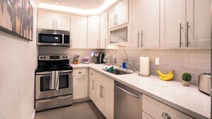 A modern kitchen with stainless steel appliances, white cabinetry, and a tiled backsplash. - Palm Springs Oasis Getaway with Mtn Views - Near Tram & Uptown. (Palm Springs)