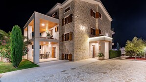 Una casa moderna de dos pisos con fachada de piedra, ventanas grandes y un espacio exterior bien iluminado.