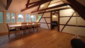 A dining area with a wooden table and chairs, large windows, and a sloped ceiling with exposed beams. - Felsenkeller Bielatal "Berthablick" (Rosenthal-Bielatal)