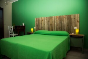 A room with a green bed, a wooden headboard, a white chair, a small table with a lamp, and a nightstand with a lamp. - La Timpa del Cucco (Roccagloriosa)