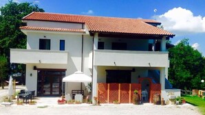 A two-story building with a red-tiled roof, a covered patio area with outdoor furniture, and a fenced entrance. - La Timpa del Cucco (Roccagloriosa)