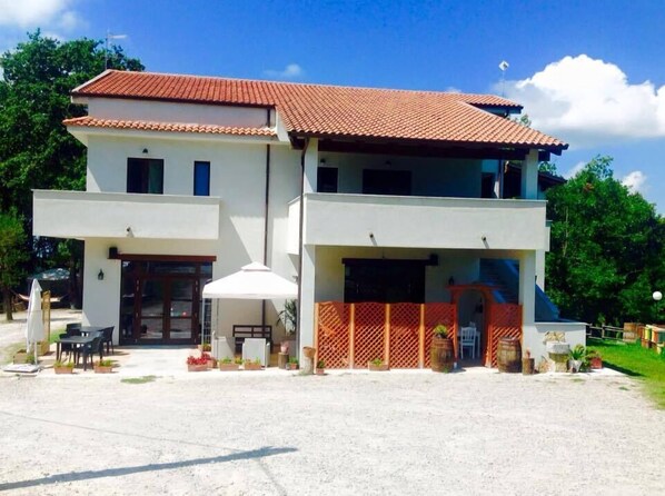 A two-story building with a red-tiled roof, a covered patio area with outdoor furniture, and a fenced entrance. - La Timpa del Cucco (Roccagloriosa)