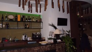 A bar area with wooden logs hanging from the ceiling, a clock, and a variety of bottles and glasses on shelves. - La Timpa del Cucco (Roccagloriosa)