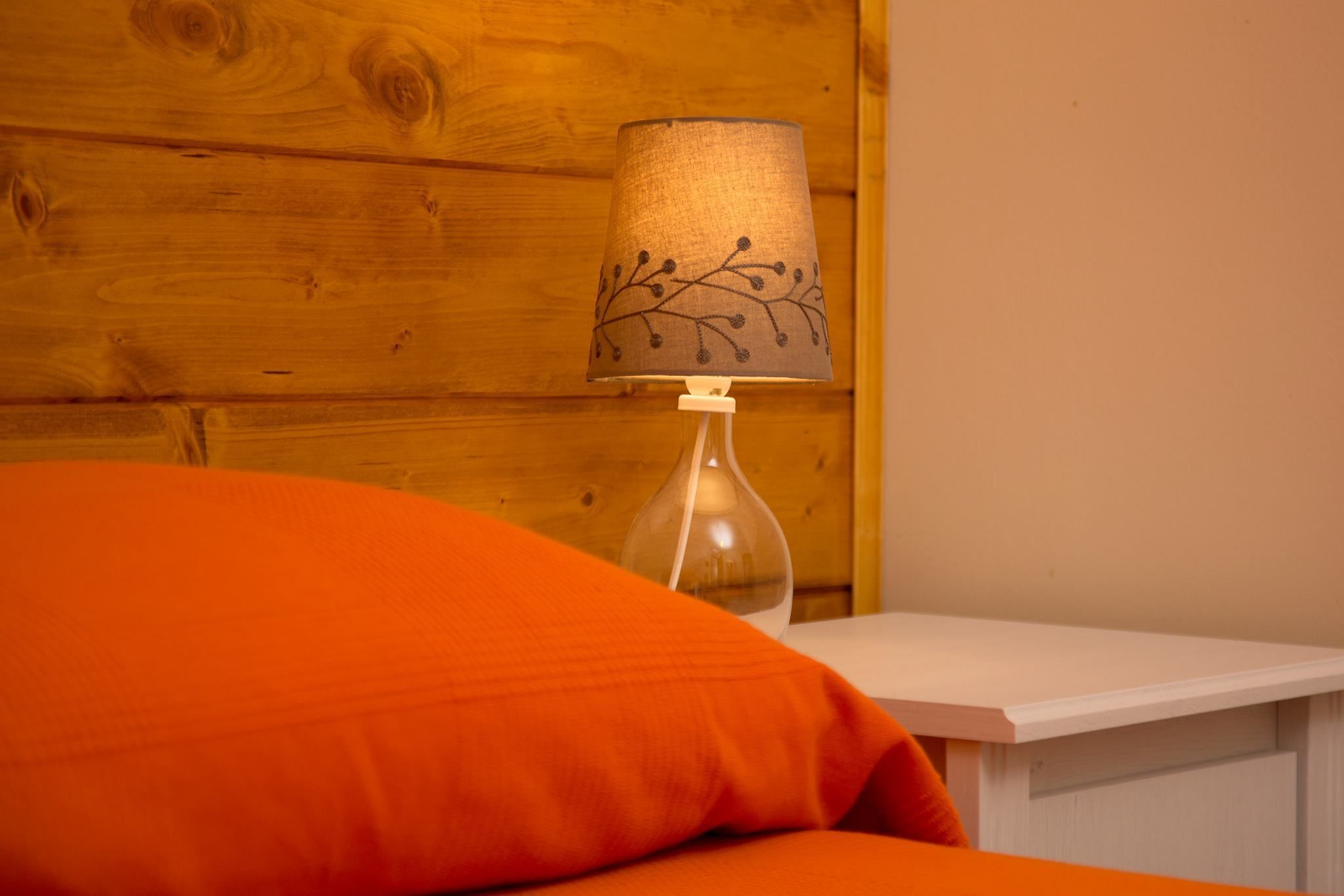 Un mur en bois, une lampe dont le pied est décoré de motifs rappelant des branches, et un coussin orange.