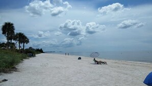 Una playa con cielo despejado, palmeras y algunas personas.
