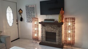 Una sala de estar con chimenea de piedra, un televisor de pantalla plana montado encima y un letrero decorativo en la pared.