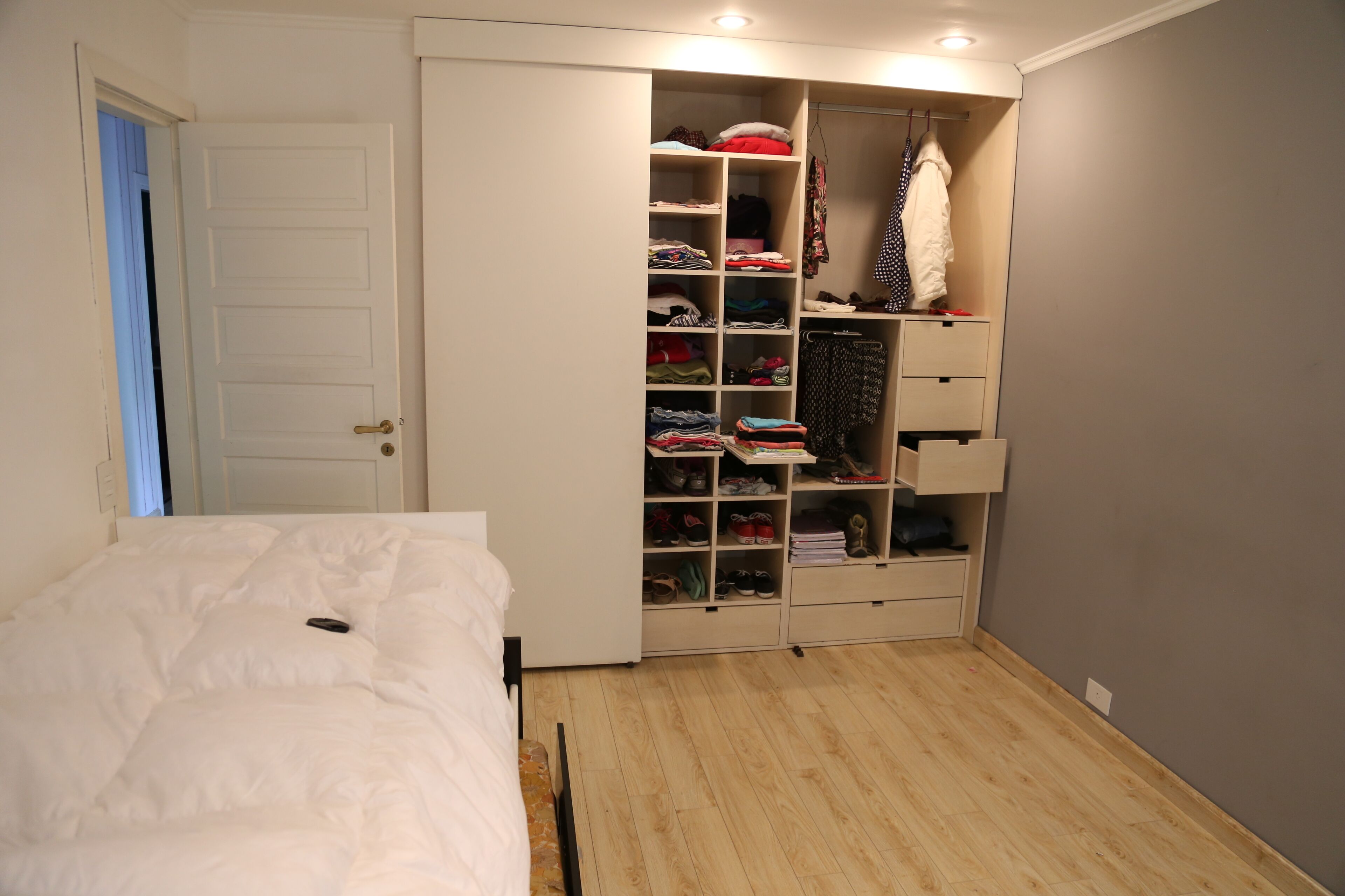 Une chambre à coucher avec un lit, une armoire avec des étagères et des tiroirs, et un plancher en bois.
