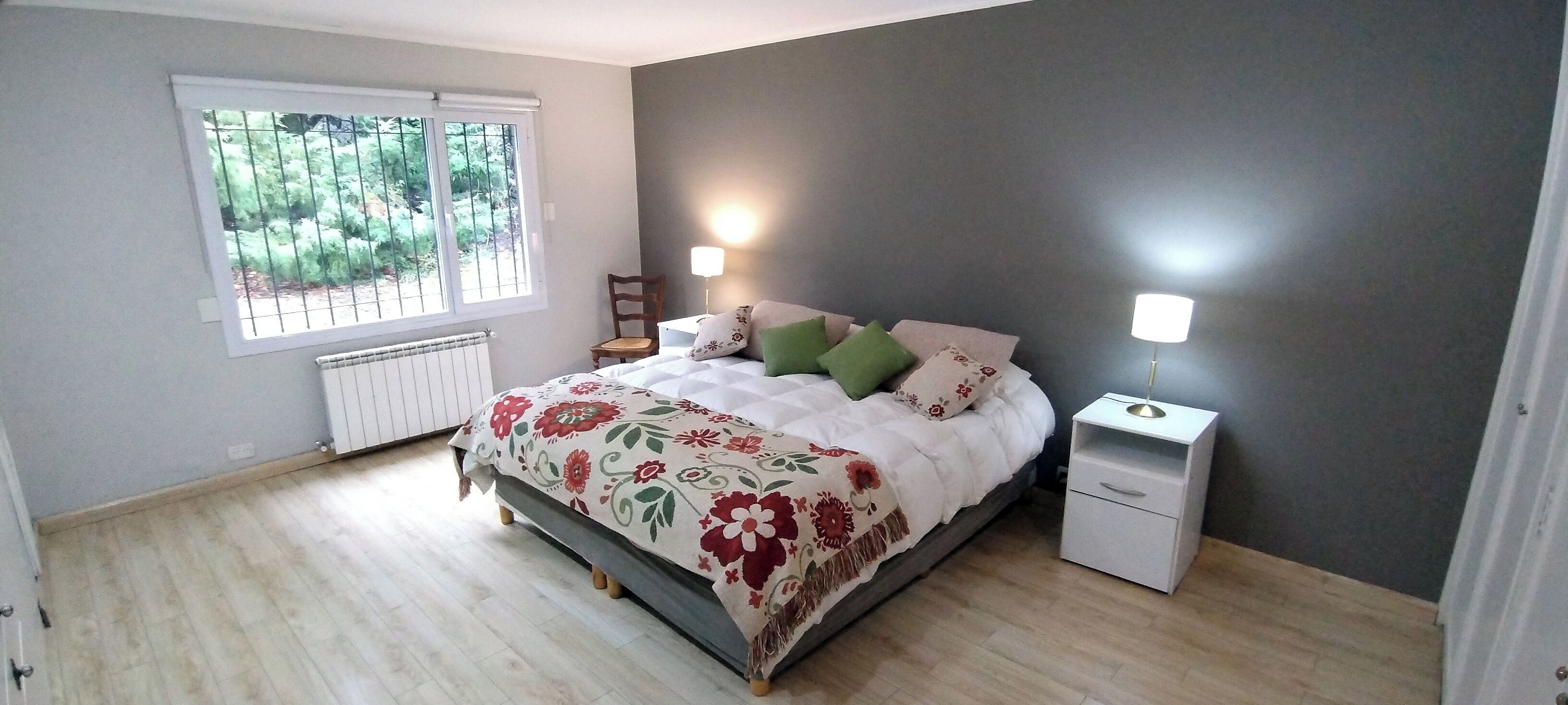 Ein Schlafzimmer mit einem Bett, zwei Nachttischen, einem Fenster mit Blick auf Grünflächen und einer Heizung.