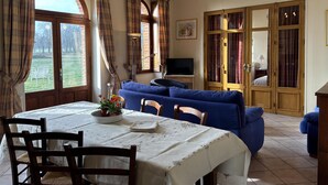 Ein Essbereich mit einem Tisch für zwei Personen, einem blauen Sofa und einem Fernseher im Hintergrund.