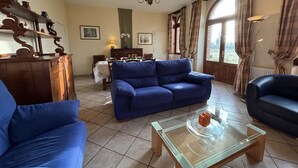 Ein Wohnzimmer mit einem blauen Sofa, einem Glastisch und einem Essbereich mit Tisch und Stühlen.