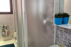 A bathroom with a glass shower door, a white sink, and two blue potted plants on a shelf.