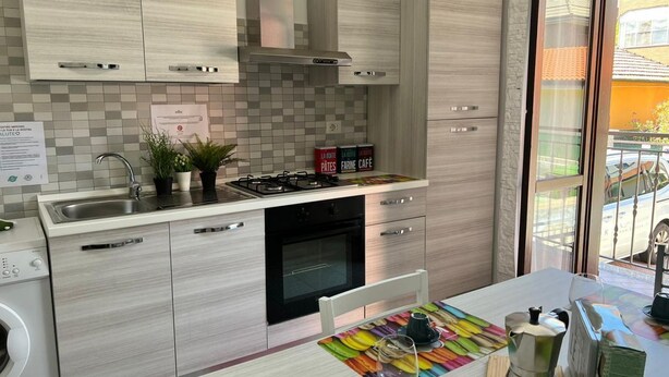 Une cuisine moderne équipée d’une cuisinière, d’un four et d’un évier intégrés. On trouve une machine à laver sur la gauche et un coin repas agrémenté d’un set de table coloré.